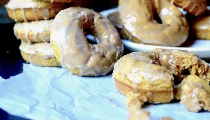 Pumpkin donuts with maple glaze propped up on one another on top of a blue napkin