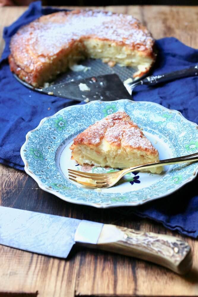 Photo of French Apple Cake, recipe by stacy lyn Harris on a blue china plate with knife in front on wood