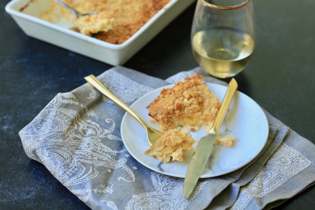 Squash casserole on a plate with fork with gray napkin under it with wine glass and casserole in background