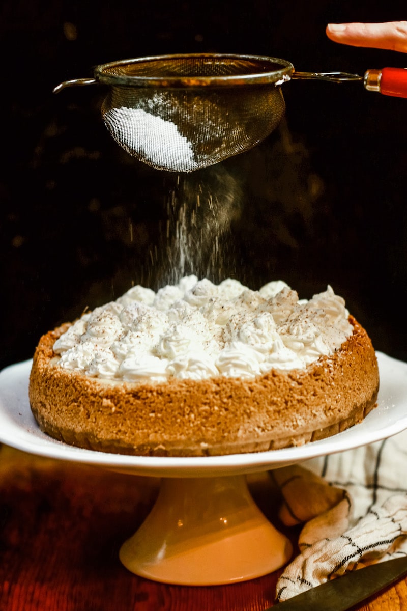 Shown with whipped cream rosettes on a white cake stand and powdered sugar being sprinkled on top