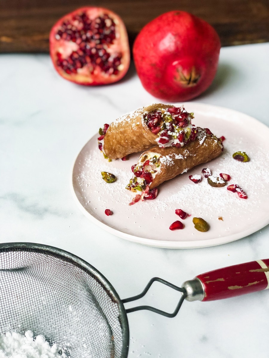 Cannoli with pomegranates in background on marble