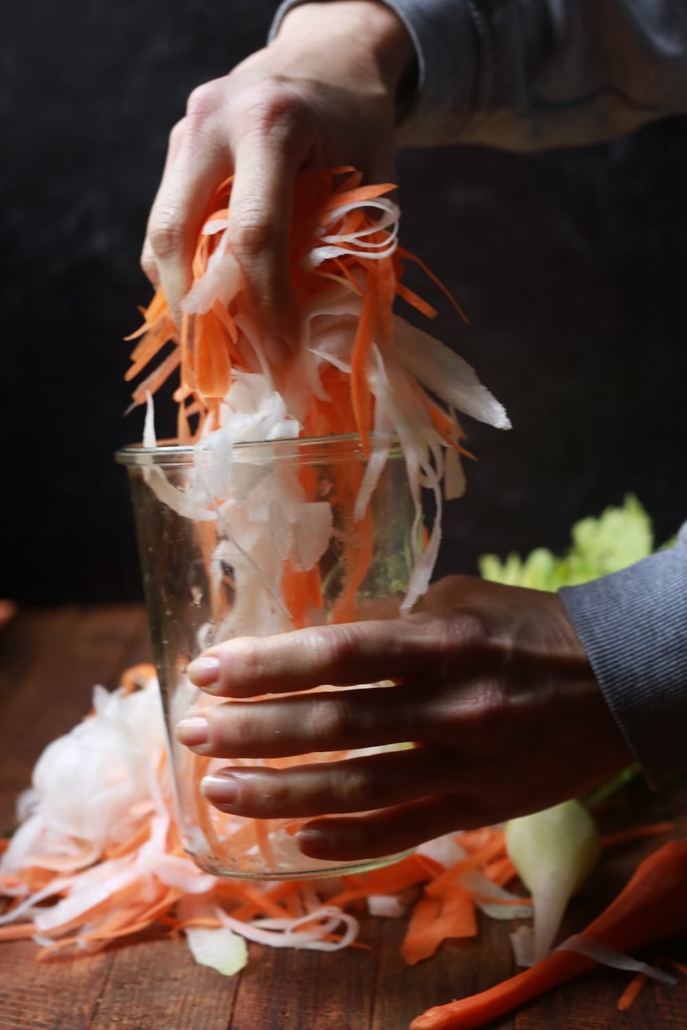 Stacy Lyn's hands putting daikon radishes and carrots in a. pickling jar