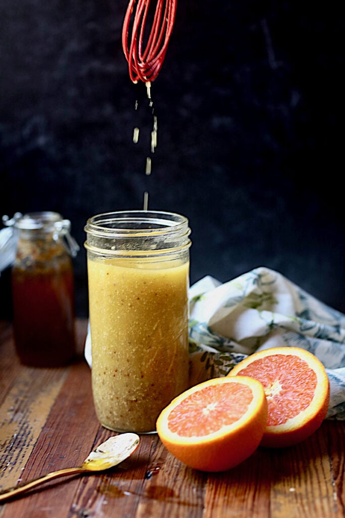 Mason jar on wood with vinaigrette with black background with oranges and honey in the photo and red whisk