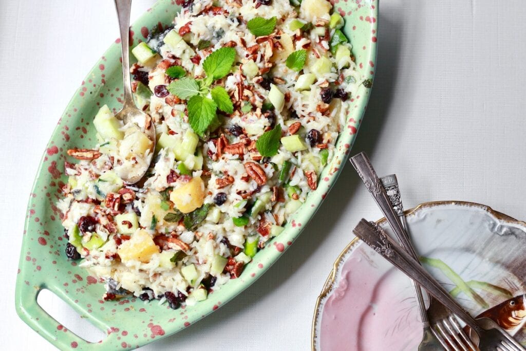 Rice Salad with pecans and pineapple with mint leaves on white background in green dish