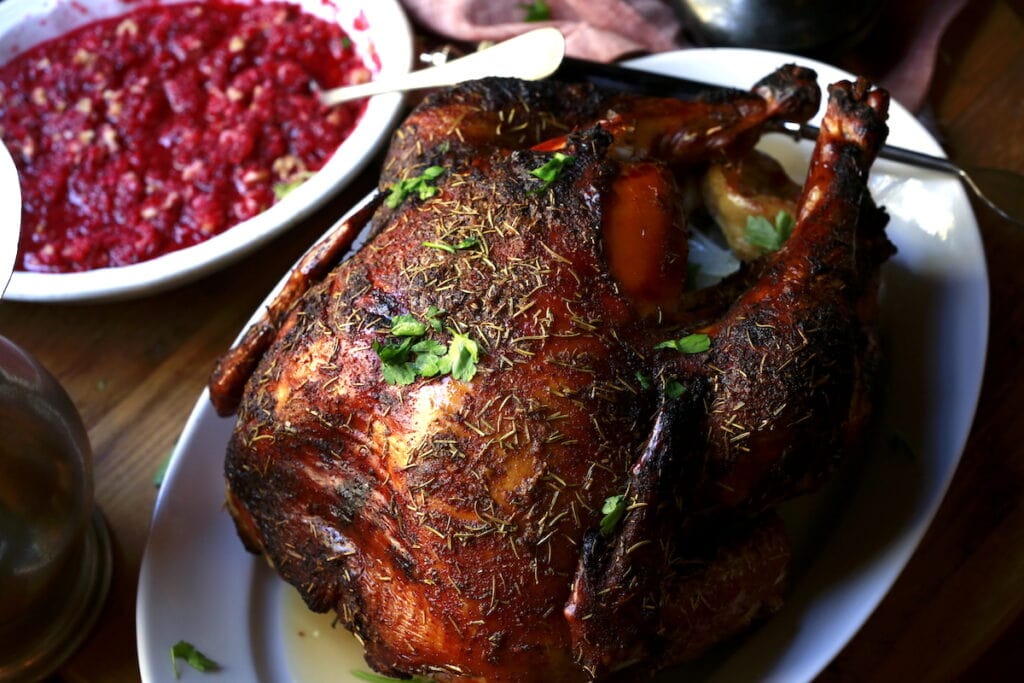 horizontal photo of whole roasted turkey with herbs and cranberry side