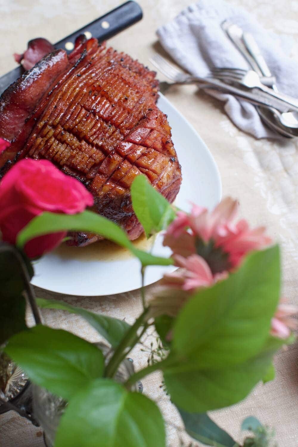 spiral glazed ham sliced on plate for Easter dinner beside arranged flowers
