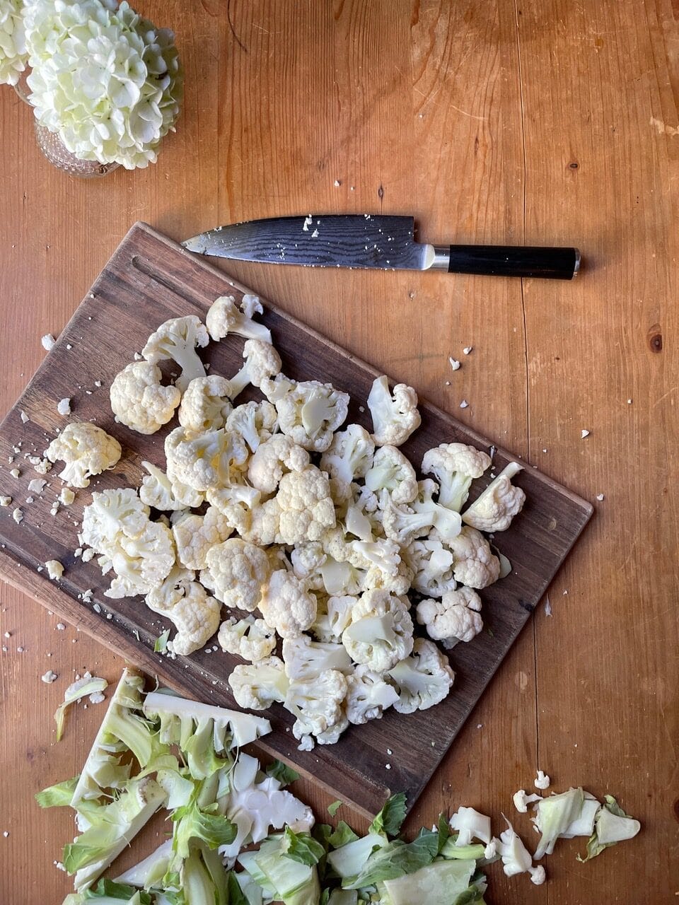 bite-sized cauliflower florets, cored, on wooden cutting board with knife and trimmings