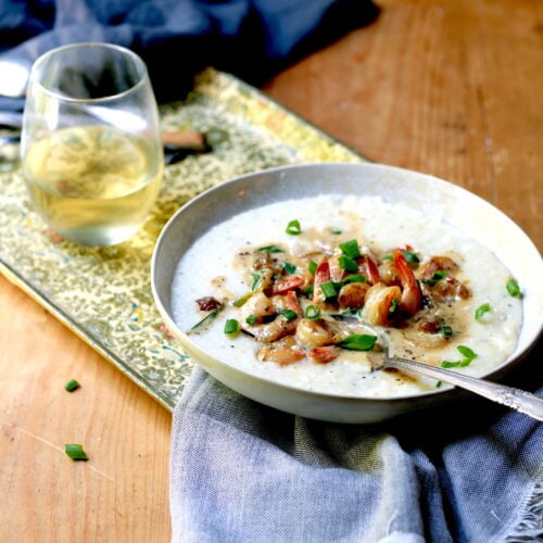 Shrimp and grits in white bowl with spoon, beverage, and napkin