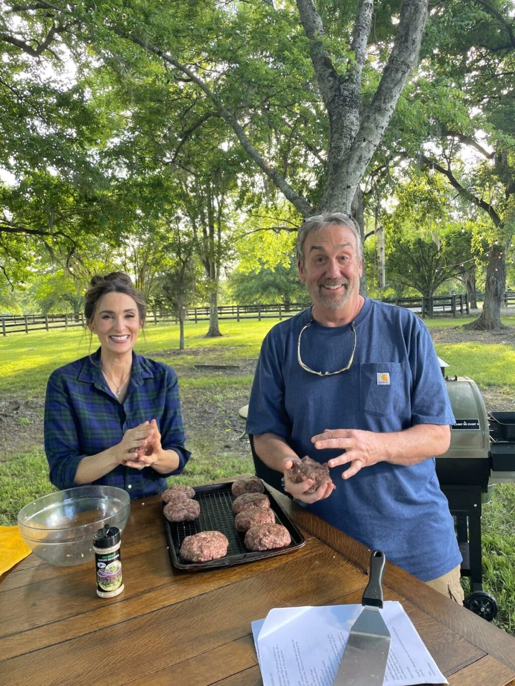 Stacy Lyn and Scott Leysath making venison burger patties outdoors on flat grill