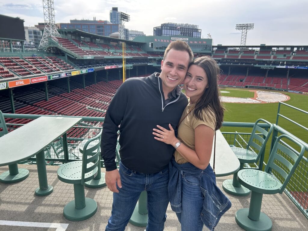 Hampton and Abbi at Fenway Stadium after getting engaged - the happy young couple standing together with a background of bleacher seats