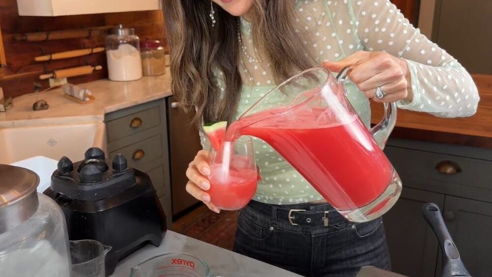 Stacy Lyn pouring a glass of fresh watermelon lemonade from pitcher in kitchen